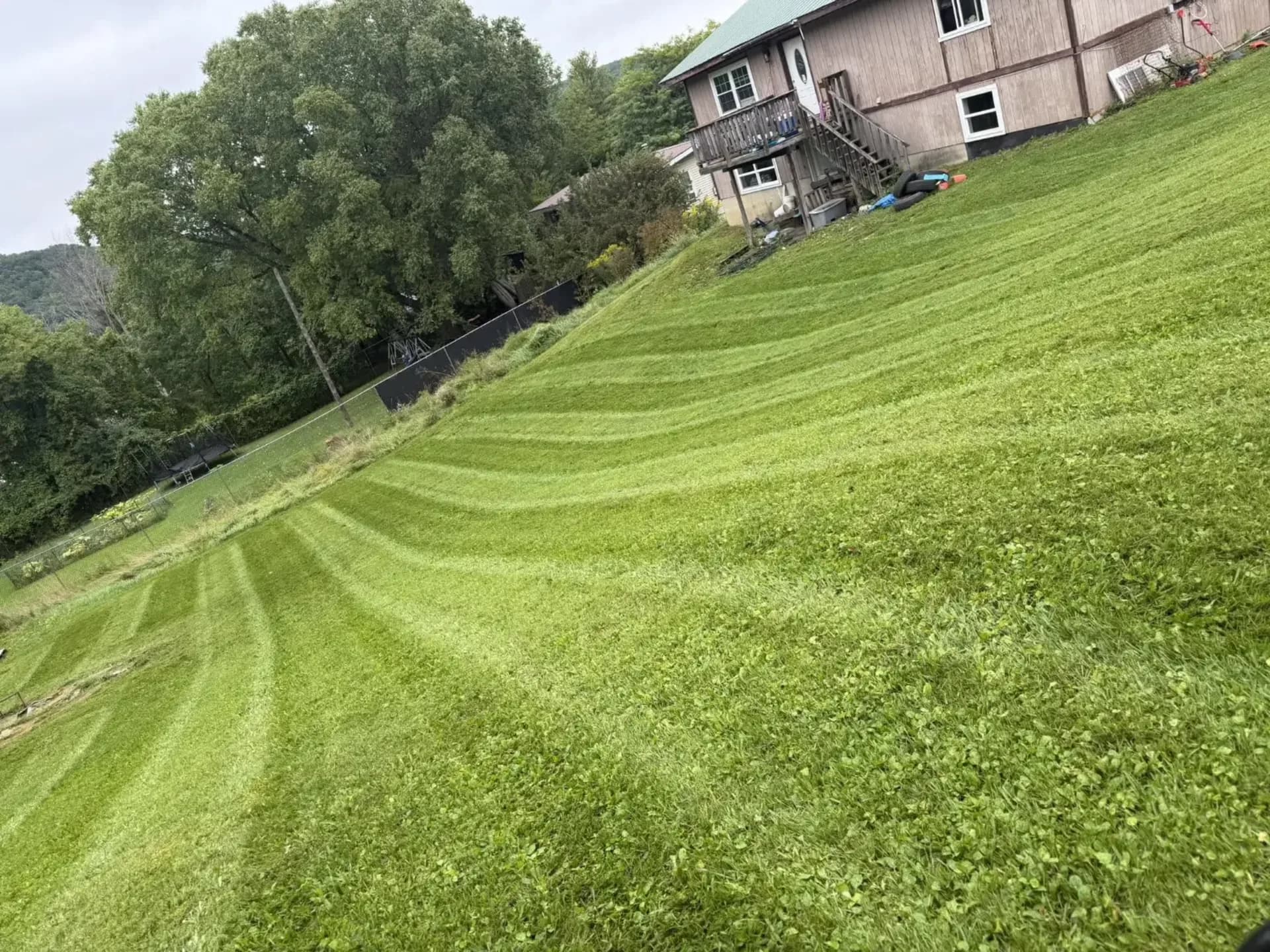 A large hillside lawn freshly mowed with clean stripes by EK Services