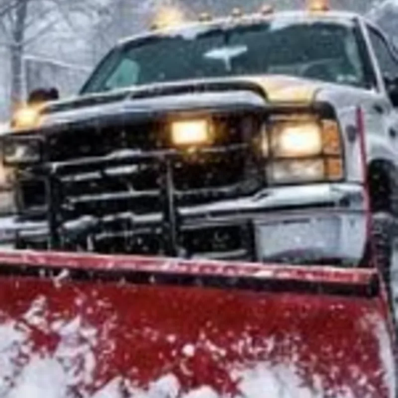 Pickup truck with a red plow blade clearing snow during a storm